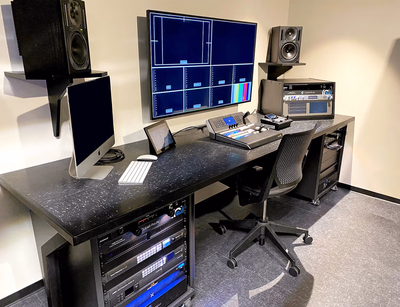 Broadcast control room with multiple screens, workstations, and rack-mounted AV equipment