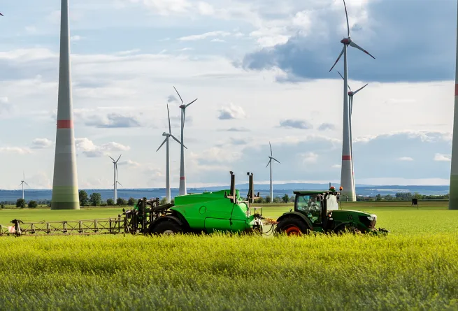 Traktor auf einem Feld vor Windenergieanlagen