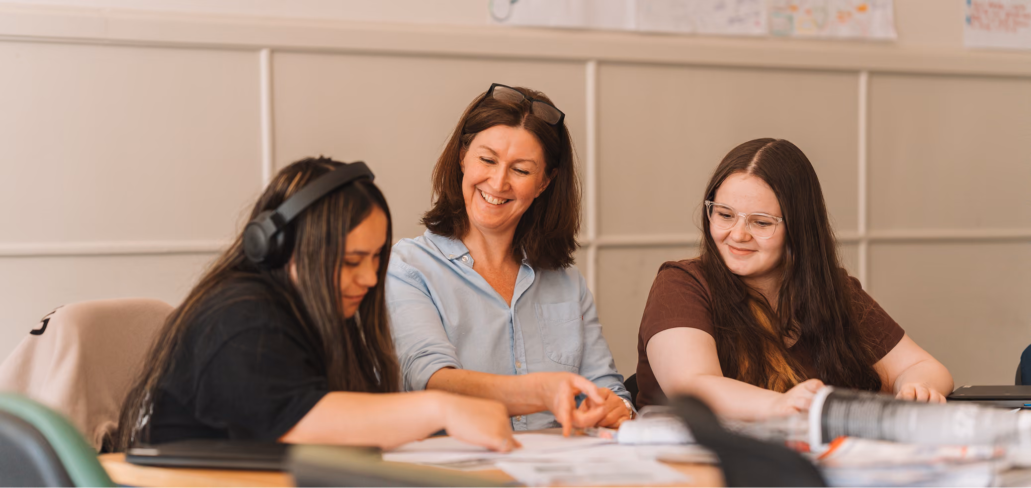 A tutor smiling with two learners at a table, working through documents together