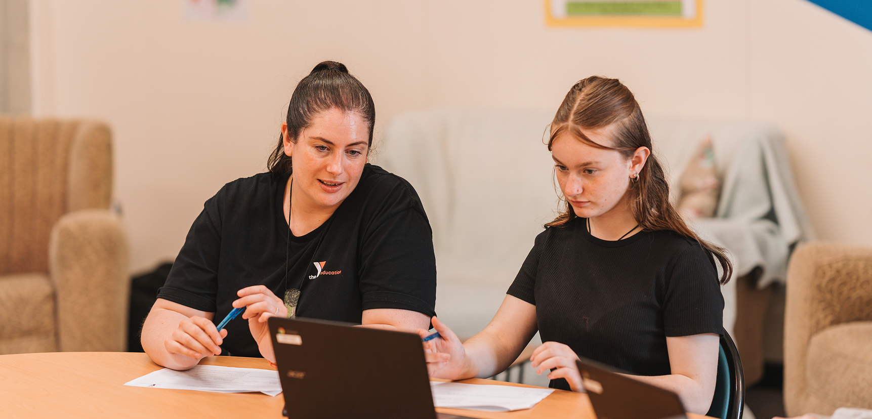 A tutor and a learner in Y Education shirts working at a table with a laptop