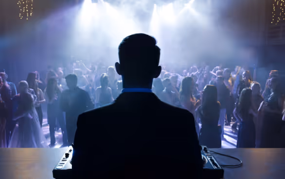 Silhouette of a DJ playing music for a crowd dancing under bright stage lights and fog.