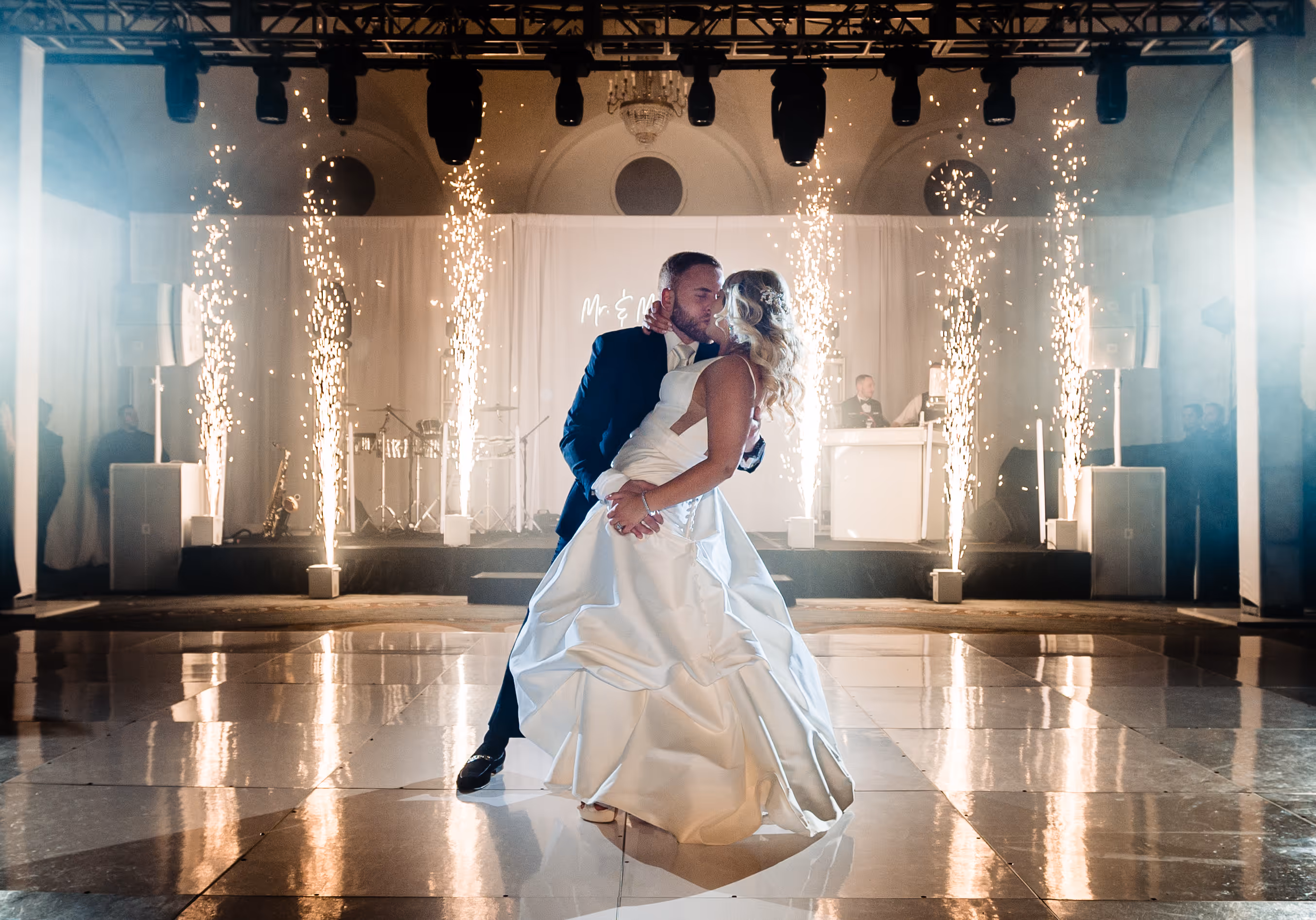 Bride and groom sharing a kiss while dancing on a shiny floor with sparklers erupting behind them.