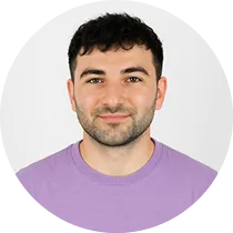 Portrait of a smiling man with short dark hair, wearing a purple shirt, on a white background inside a circular frame