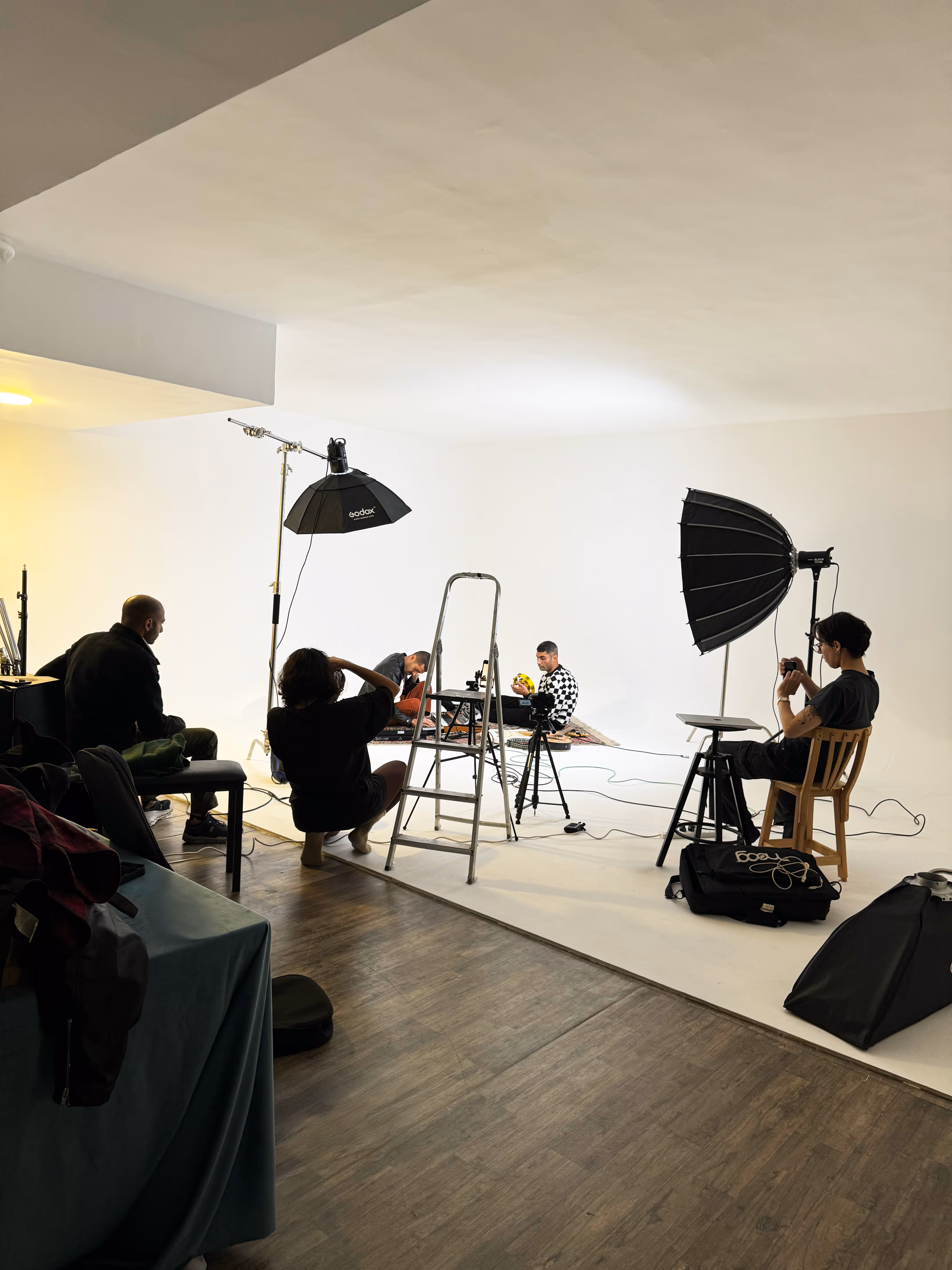 Smiling female artist sitting on the floor surrounded by acrylic paint tubes, brushes, and painted portraits on stands.