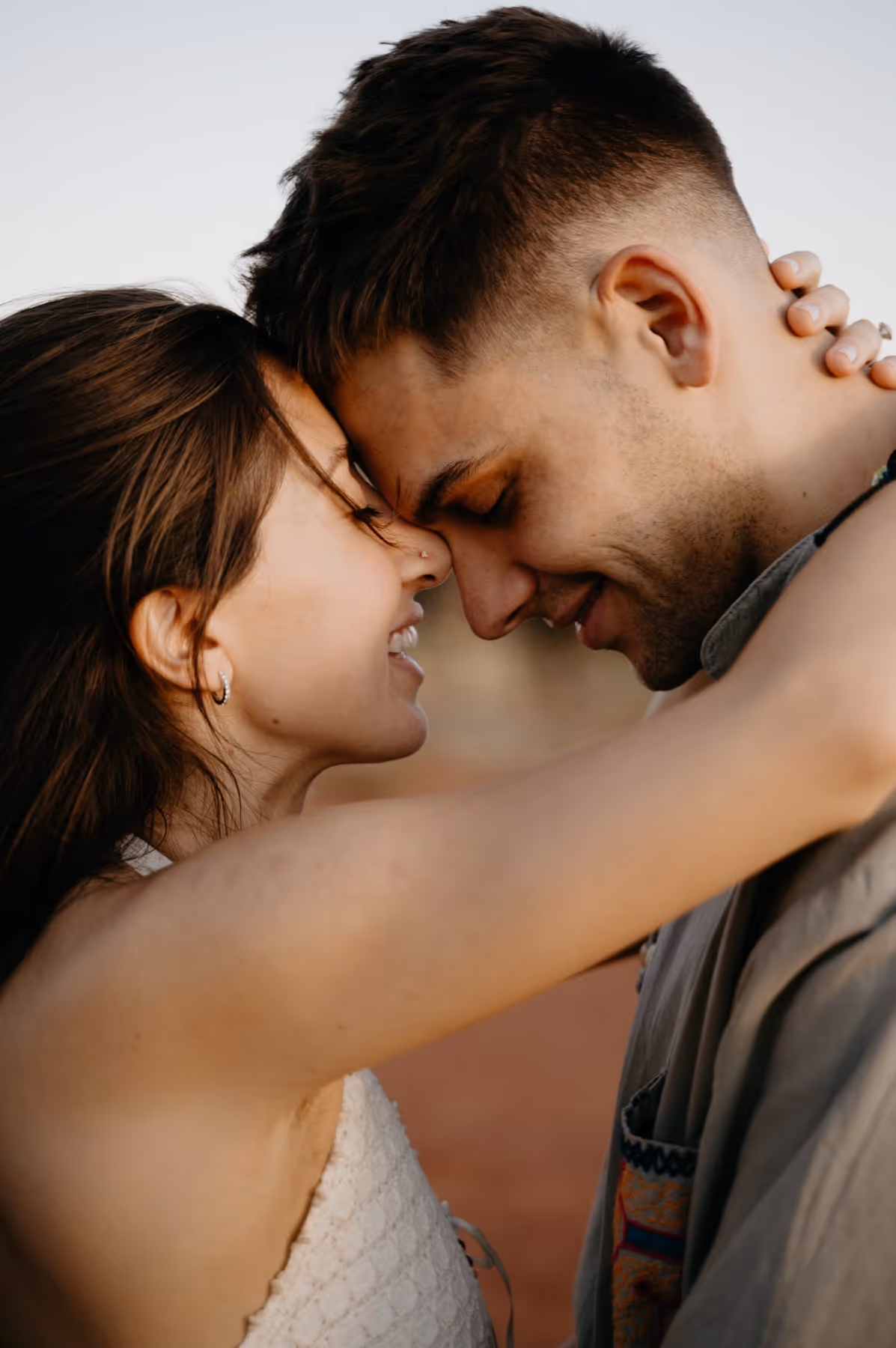 Close-up of a couple smiling with their foreheads touching and the woman’s arm around the man’s neck.