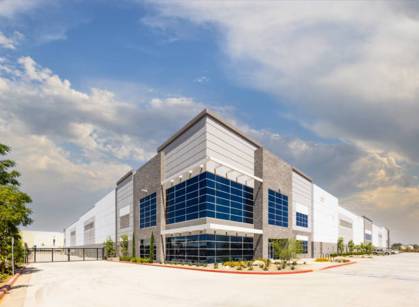 Modern industrial warehouse building with large glass windows under a partly cloudy sky.