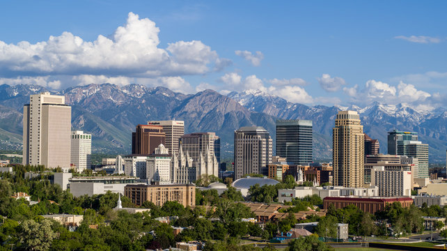 Skyline of Salt Lake City with modern buildings and the Wasatch Mountains in the background under a blue sky with clouds.