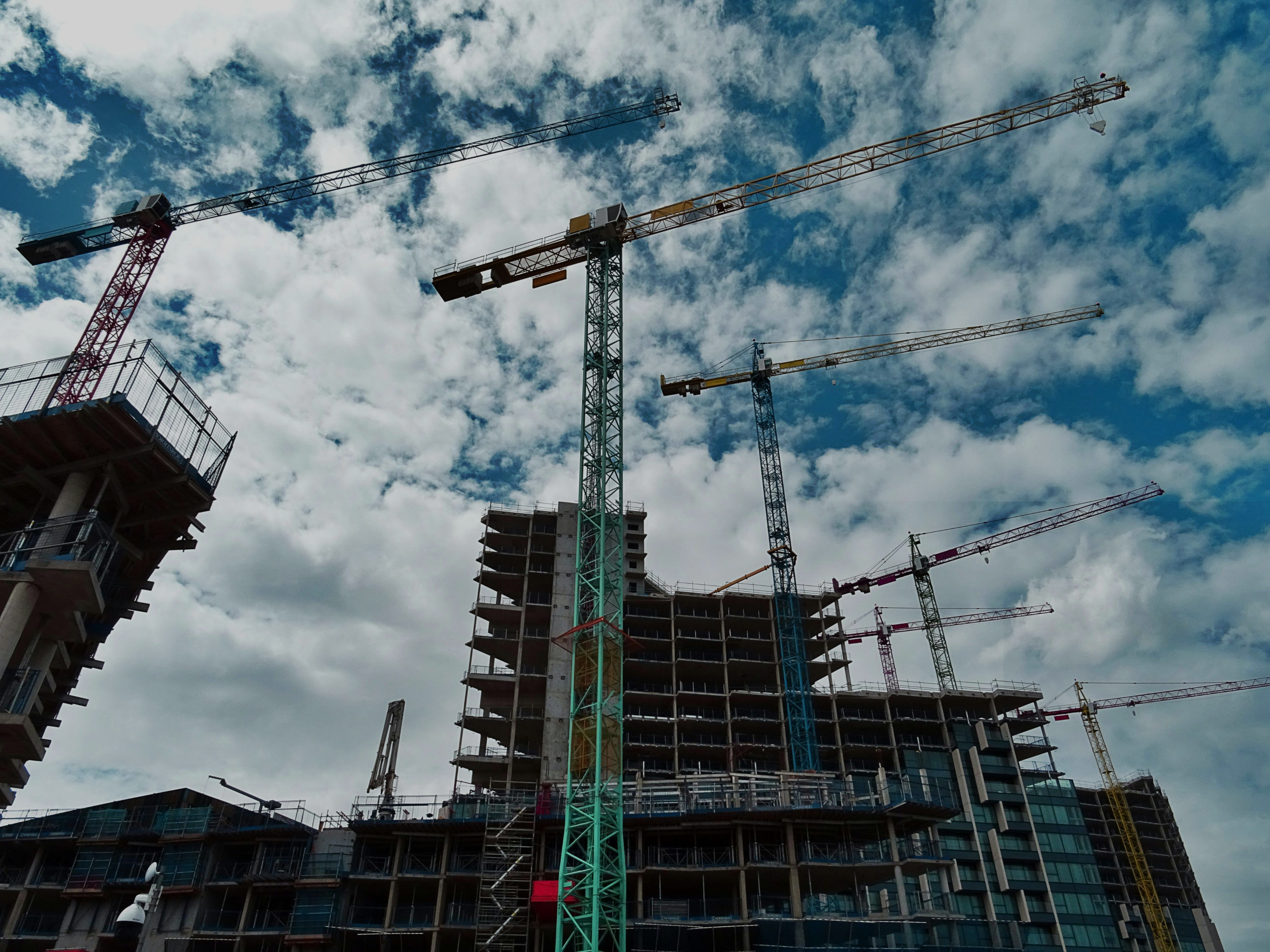 Multiple tower cranes surrounding a high-rise building under construction against a partly cloudy sky.