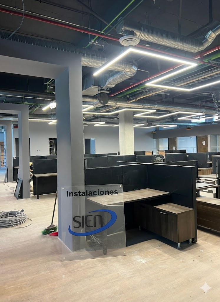 Modern office space under construction with cubicles and a transparent sign reading 'Instalaciones SIEN' leaning against a column.