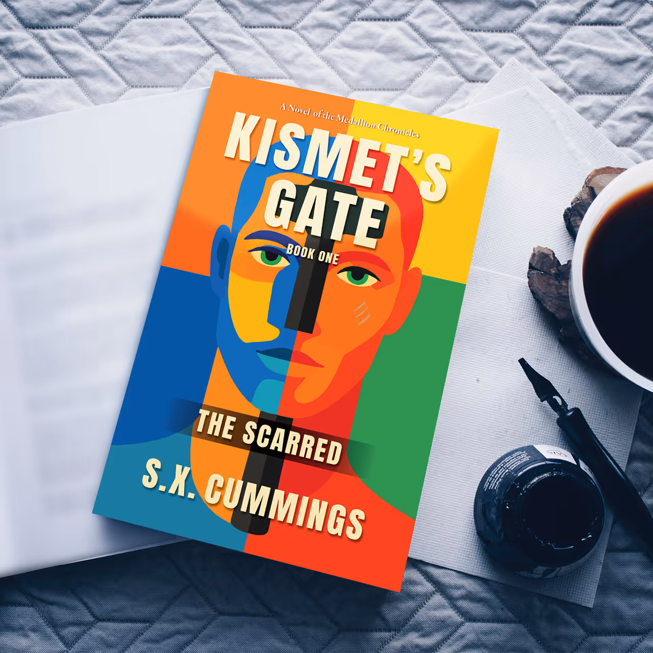 Book titled 'Kismet's Gate: The Scarred, Book One' by S.K. Cummings with a colorful abstract face cover, placed on an open book next to a cup of black coffee, ink bottle, and a pen.
