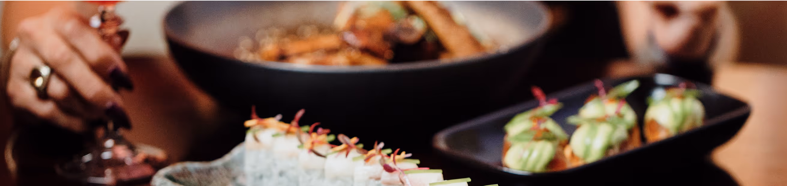Close-up of assorted sushi rolls and appetizers with avocado topping, served in black dishes during a dining experience.