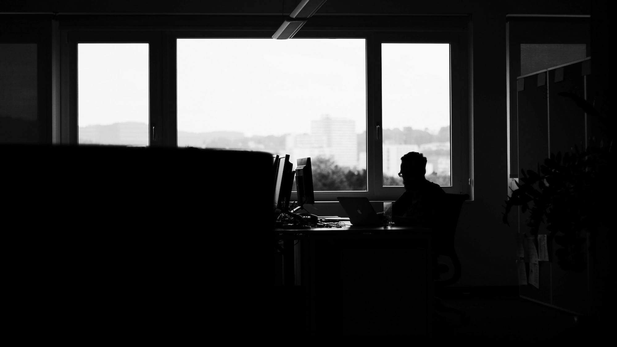 Black and white image of web design studio in Newcastle with silhouette of man working on computer with big window behind him