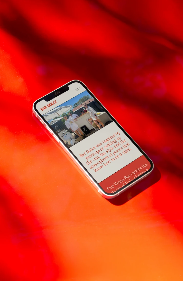 Smartphone displaying a webpage for Bar Dolce with an image of two people standing outside under umbrellas, on a vibrant red background.