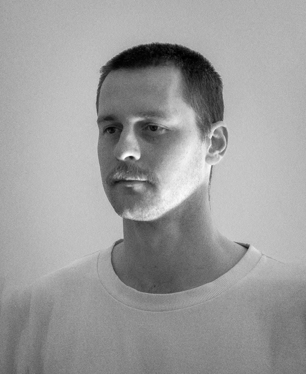 Black and white portrait of a man with short hair and a mustache wearing a plain light-colored shirt.