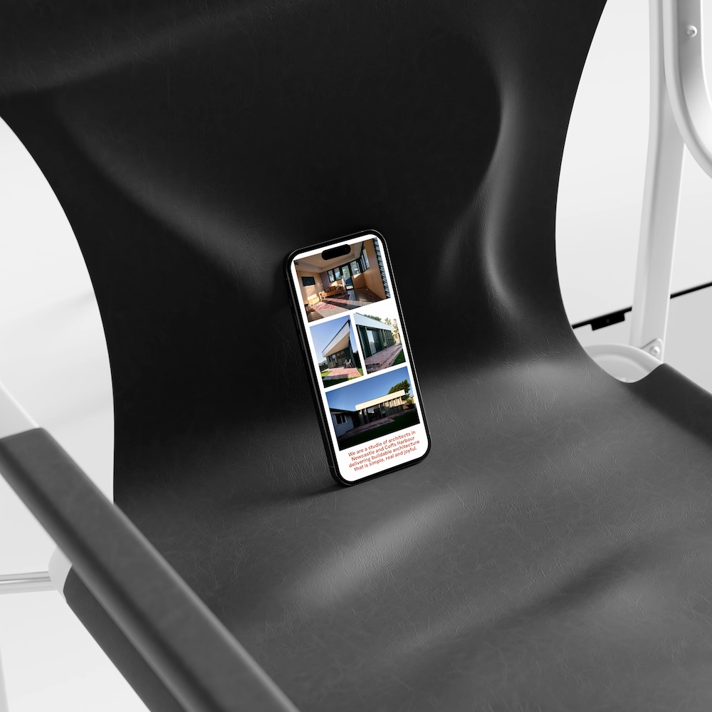 Smartphone leaning against the backrest on a black modern chair, displaying an architectural portfolio with four images of building interiors and exteriors along with a description at the bottom.