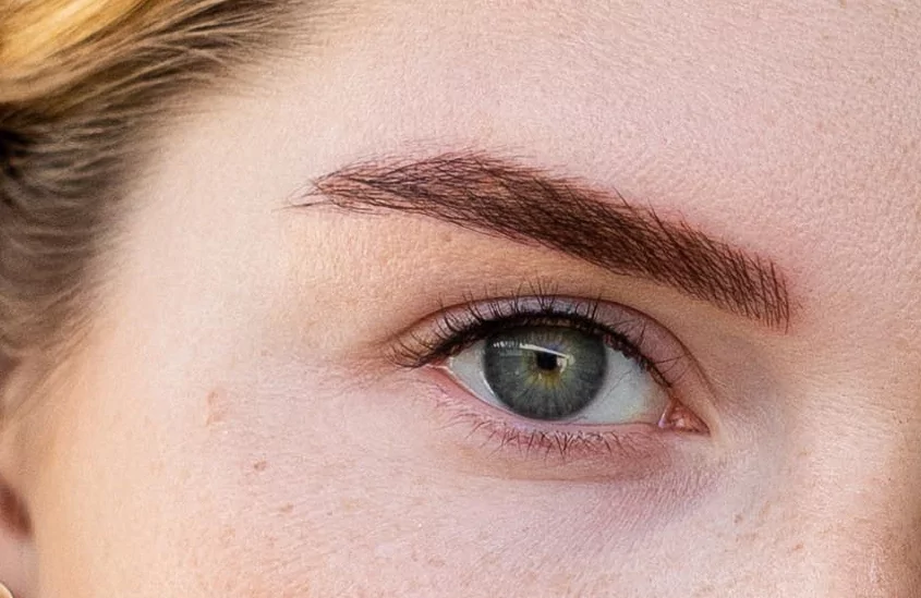 A close up of a woman's blue eye with brown hair.