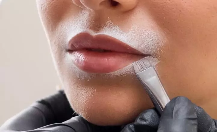 A woman is shaving her lips with a brush.