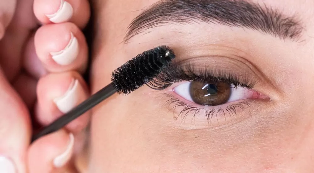 A woman is putting mascara on her eye.