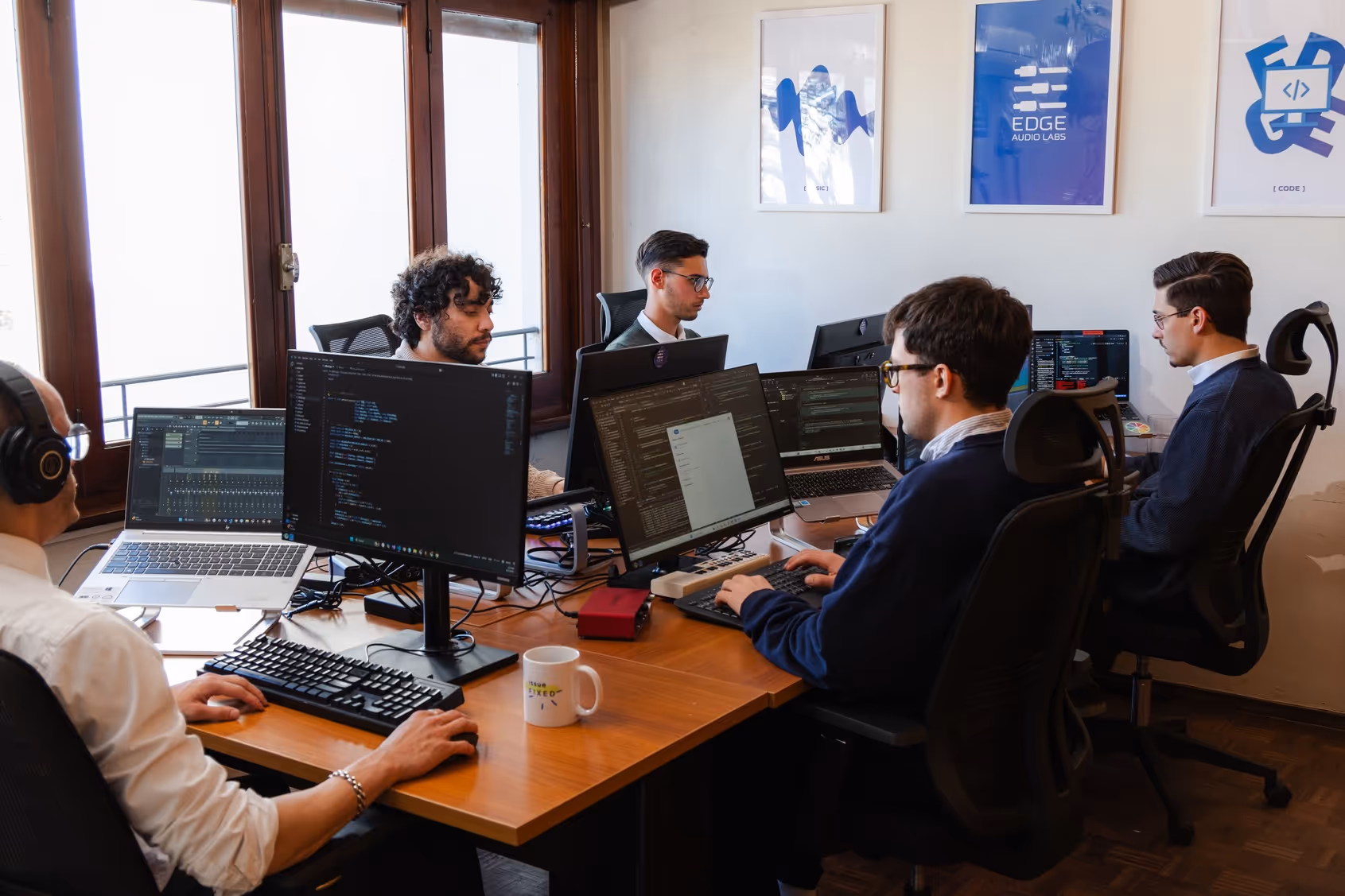 Edge Audio Labs team members working together in the office, programming and testing audio software on multiple computer screens in a collaborative workspace.