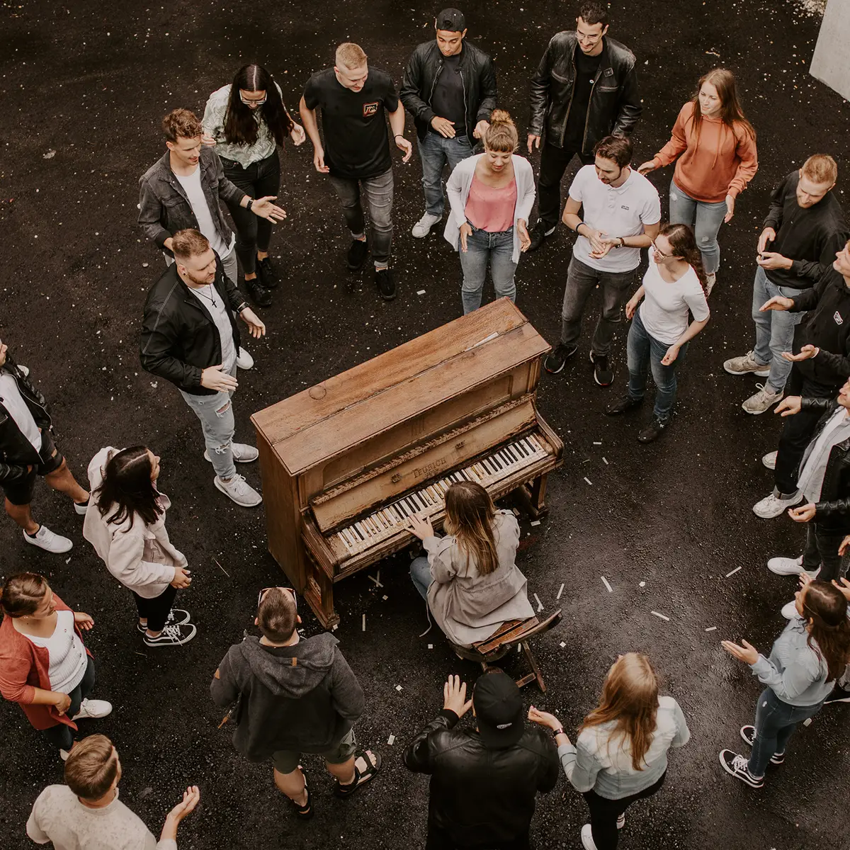 Gruppe von jungen Menschen die um ein altes Klavier versammelt sind