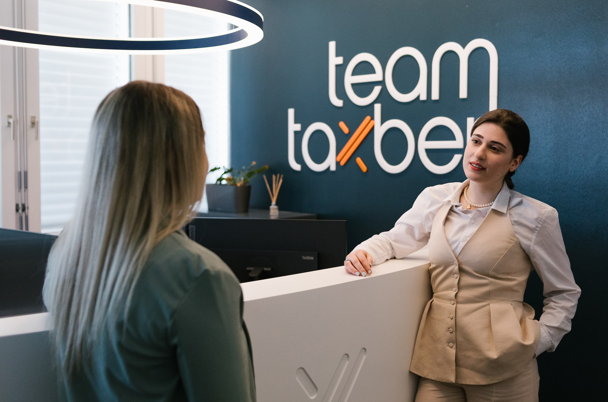Eine Frau betritt die Firma Taxbert und spricht mit einer Mitarbeiterin. 