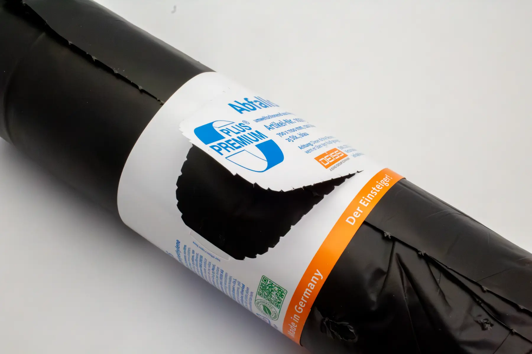 Rolled black plastic garbage bags with a white label featuring blue and orange text, including 'Plus Premium' and 'Made in Germany'.
