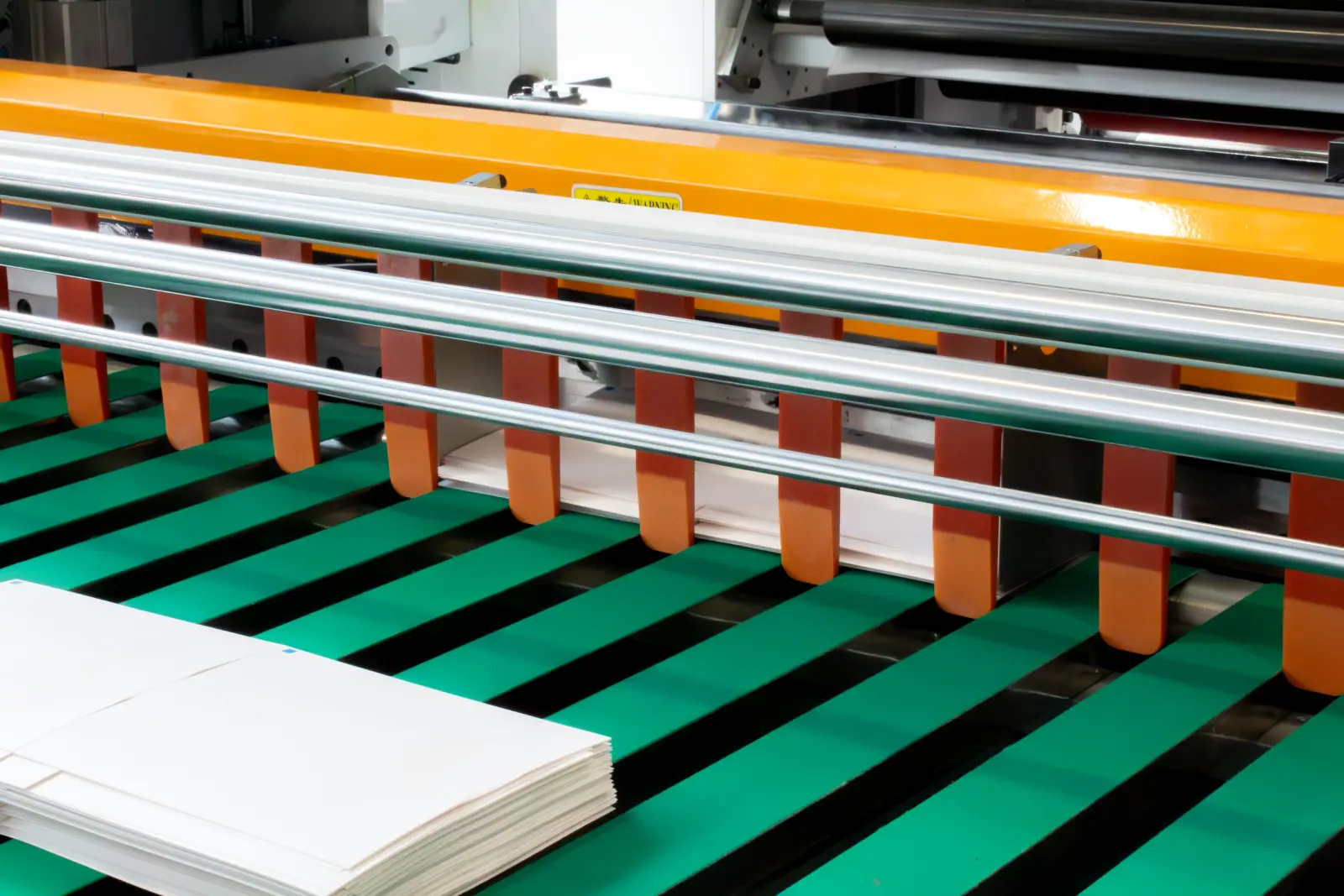 Industrial machine cutting stacked white sheets of paper on a green conveyor belt.