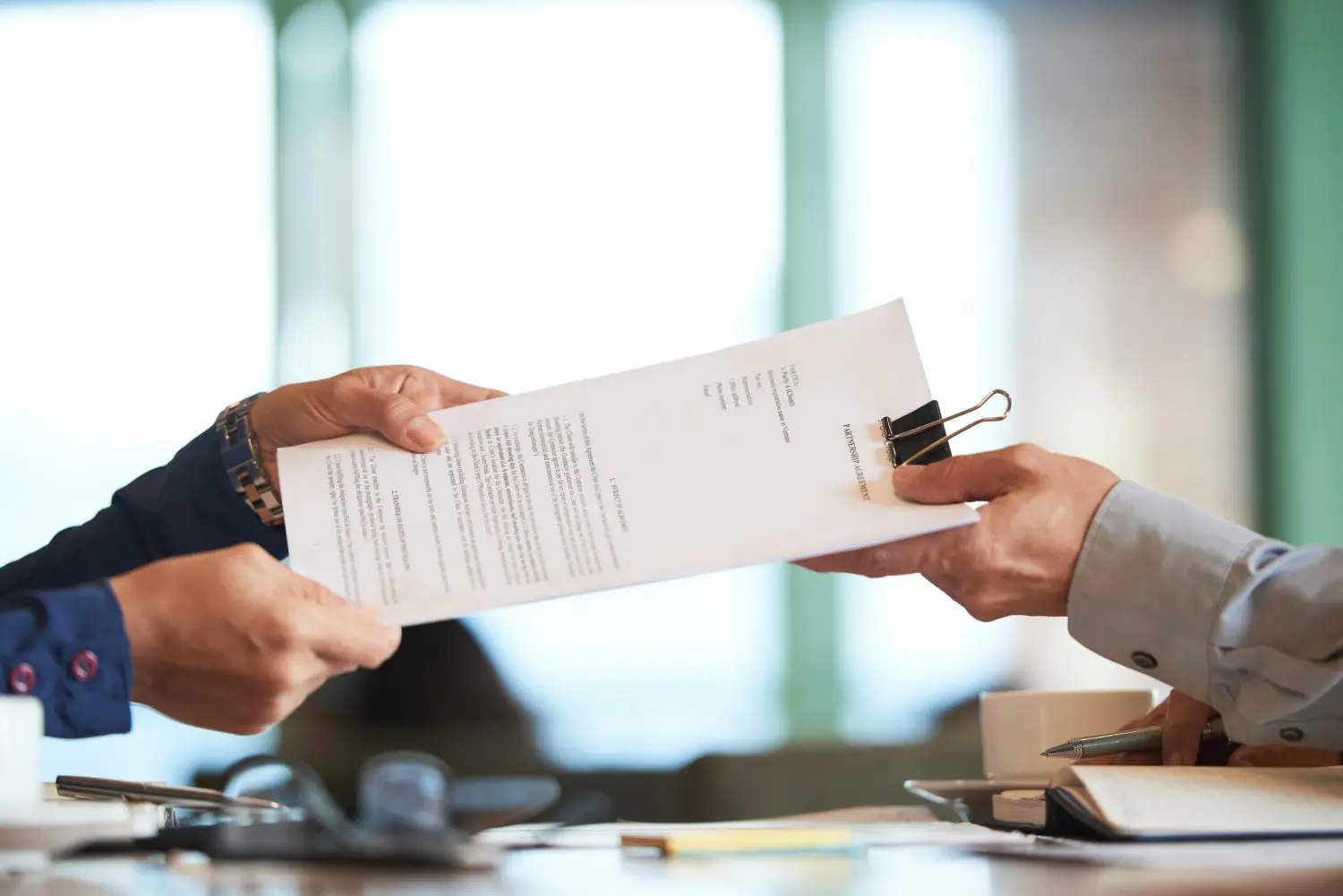 Two people exchanging a document with a binder clip in a bright office setting.