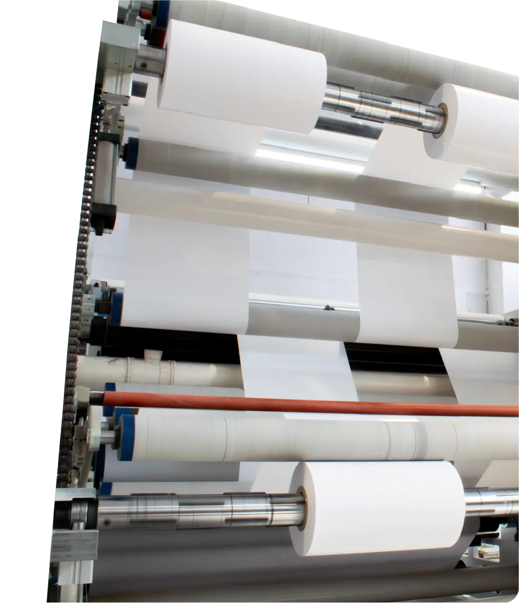 Close-up of a printing or packaging machine with several large white paper rolls on metal rollers.