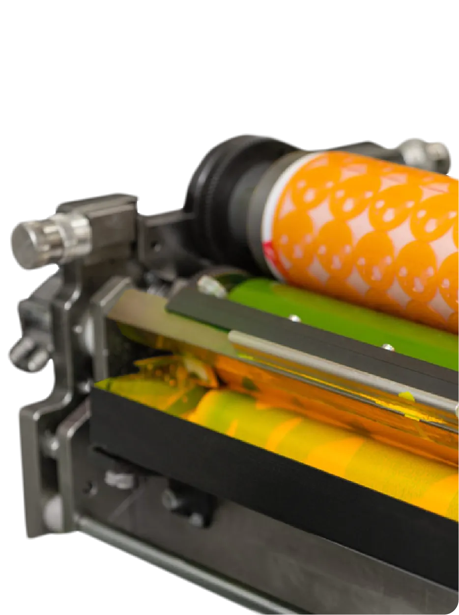 Close-up of a printing press roller with orange ink patterned with repeated skull designs.