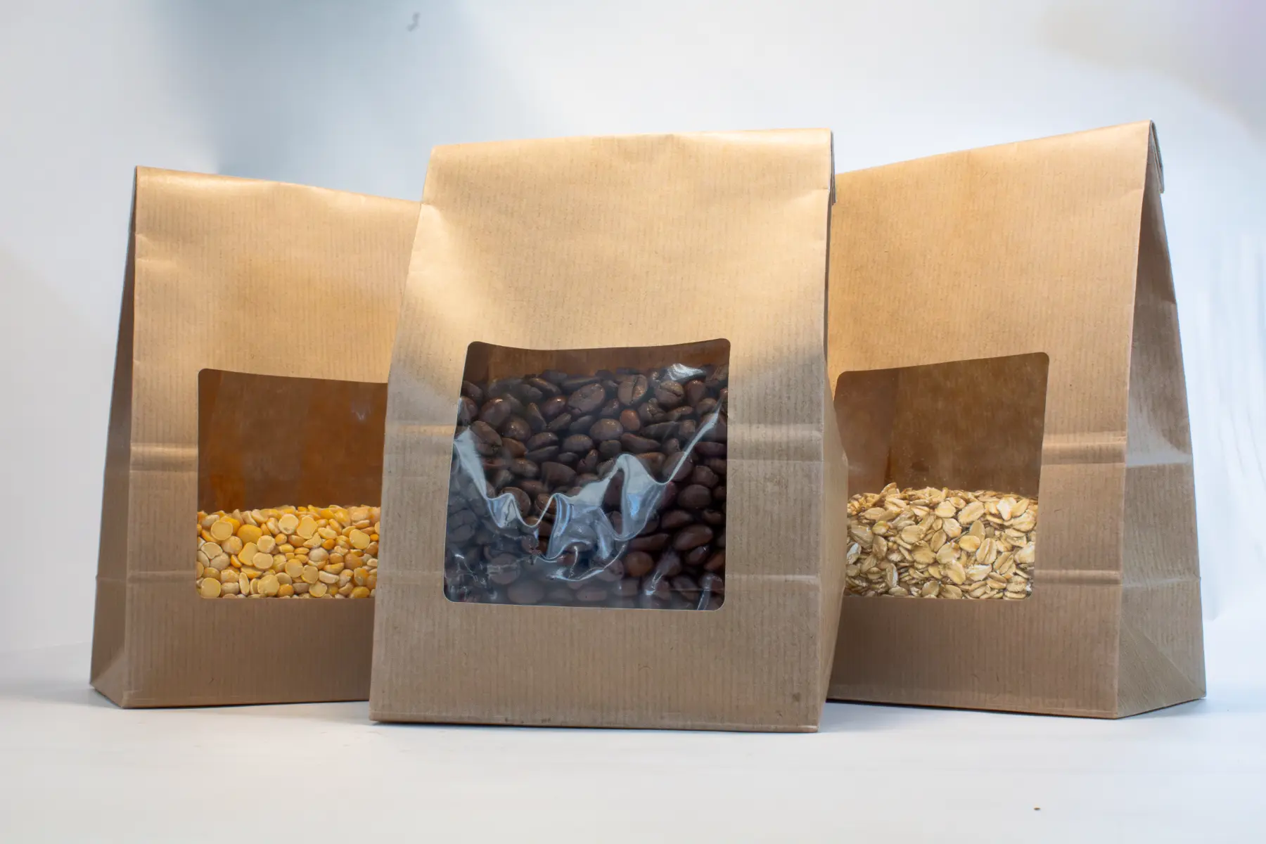 Block bottom kraft paper bags with transparent windows displaying coffee beans, lentils, and grains.