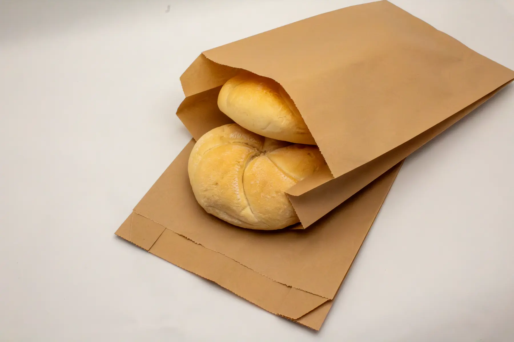 Open flat bottom kraft paper bag filled with fresh bread rolls.