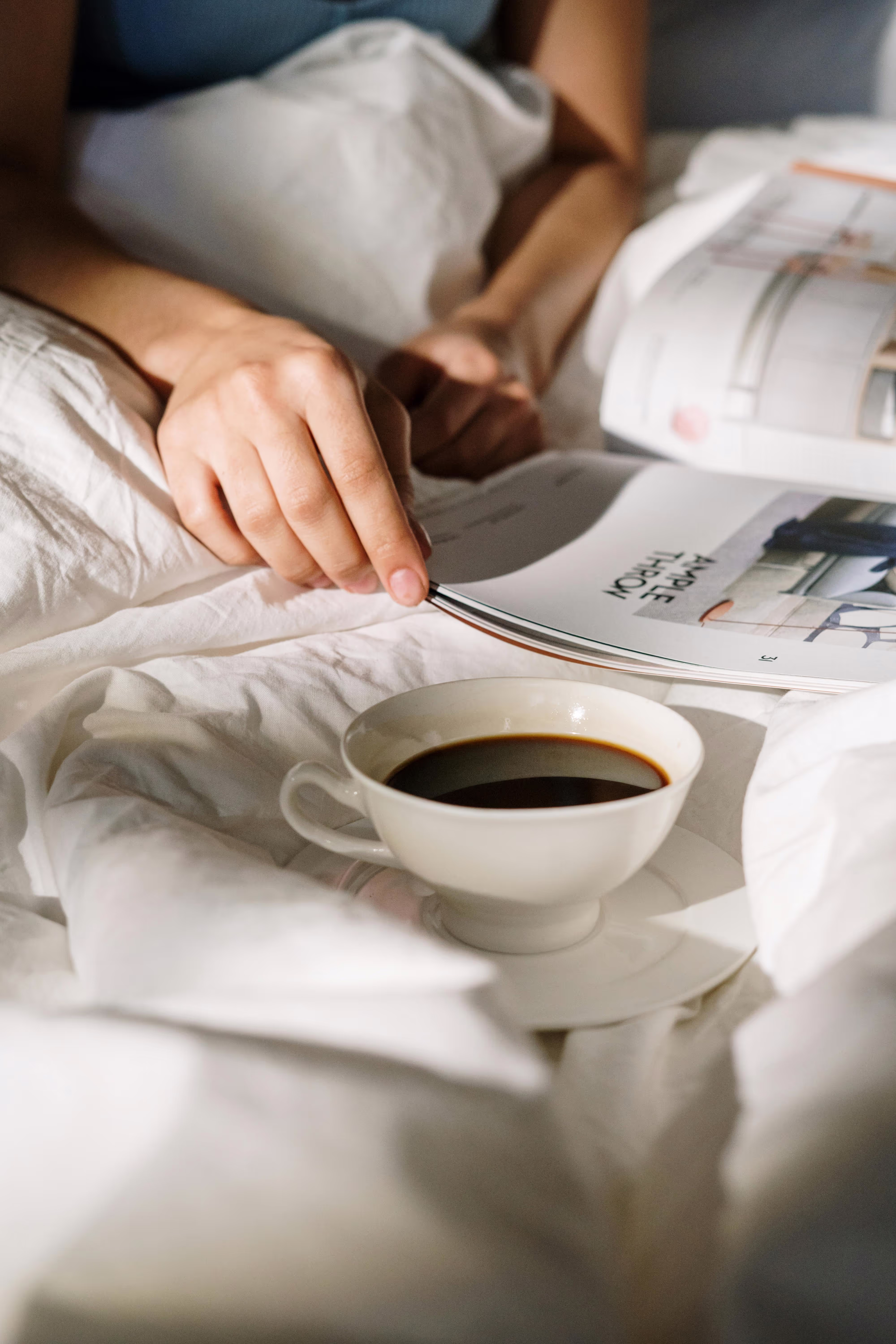 A cup of coffee and a magazine in bed.