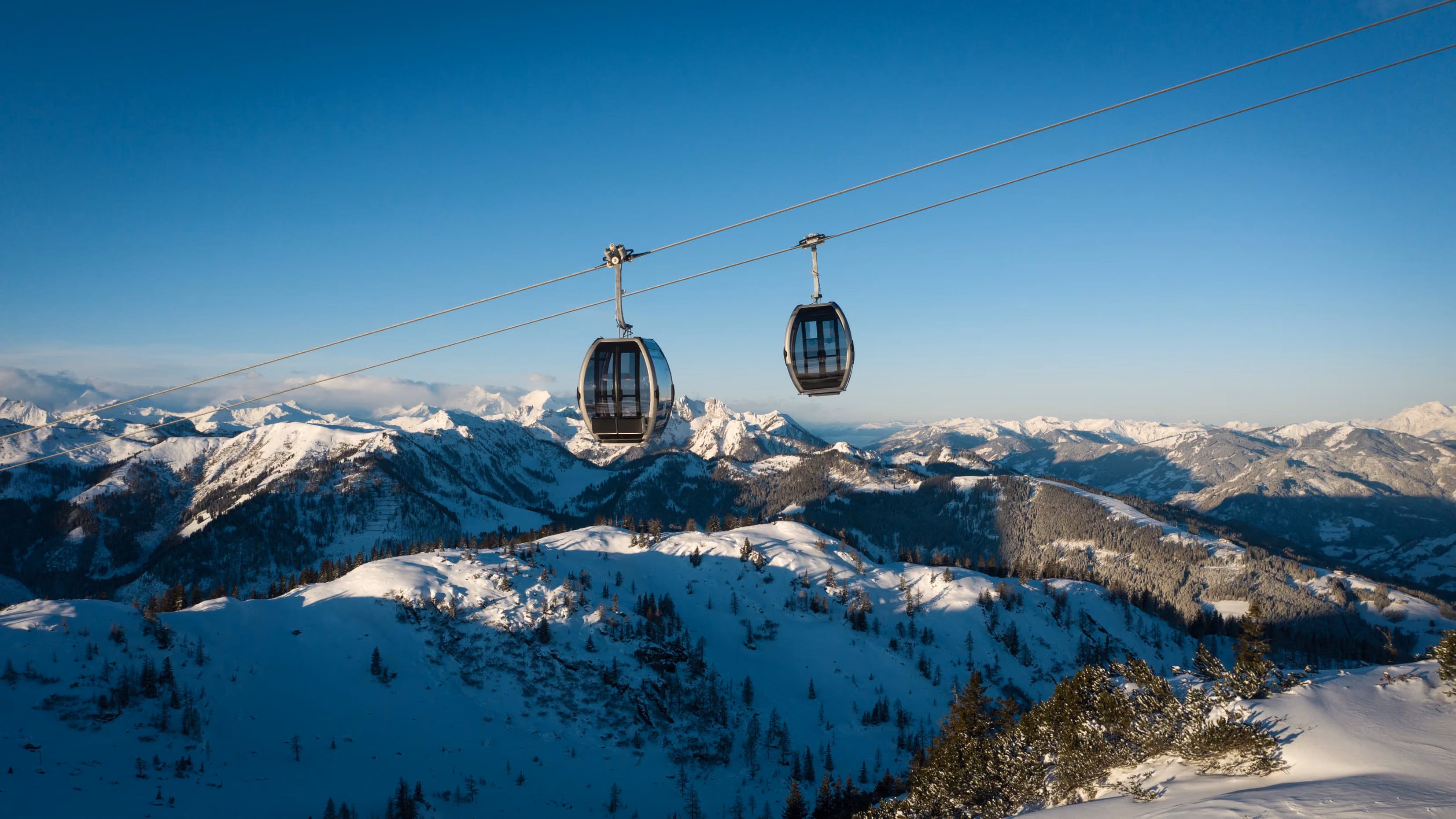 Zwei Gondeln der Shuttleberg-Bahn fahren über verschneite Alpenlandschaft bei klarem Winterhimmel