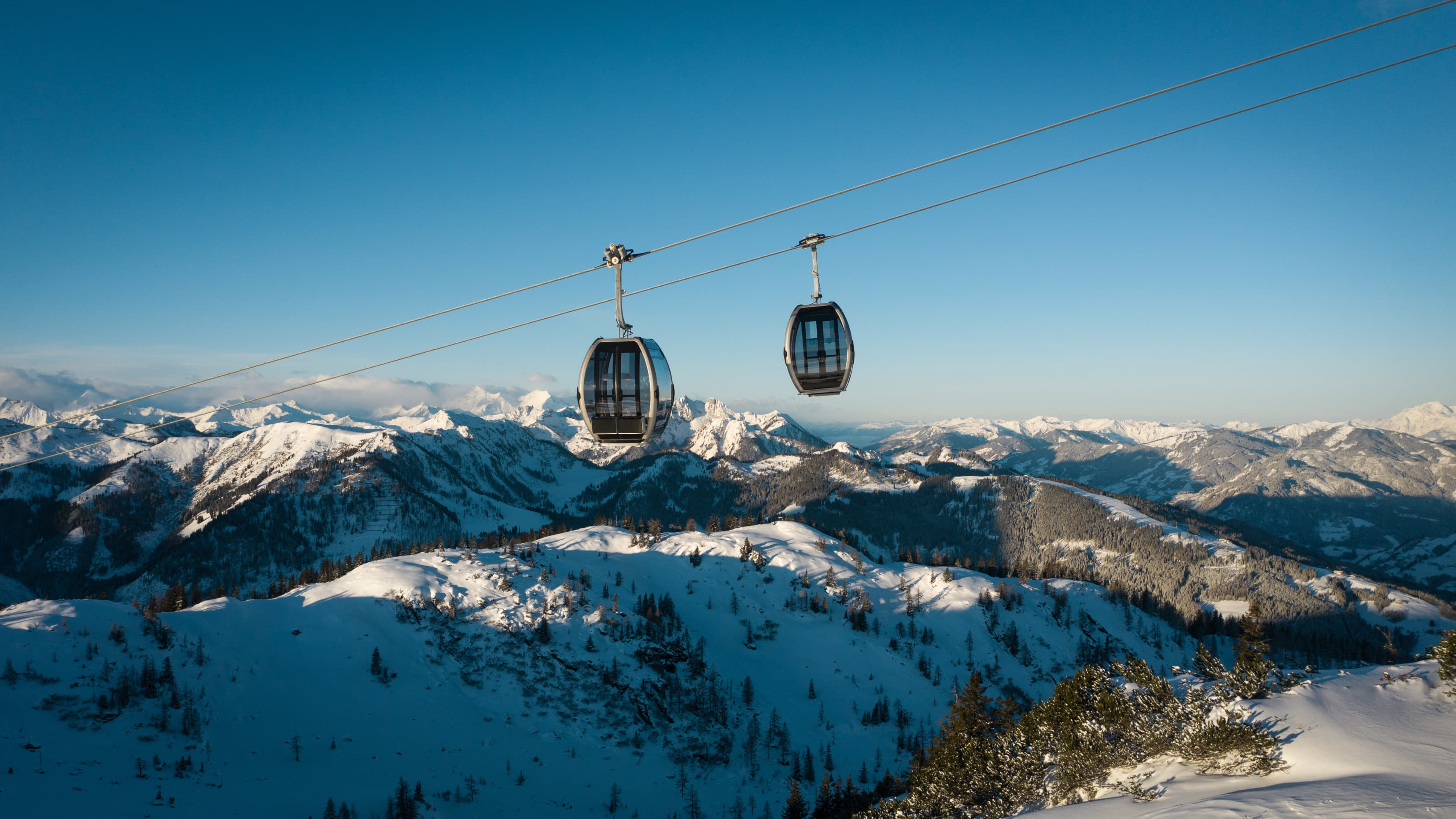Zwei Gondeln der Shuttleberg-Bahn fahren über verschneite Alpenlandschaft bei klarem Winterhimmel