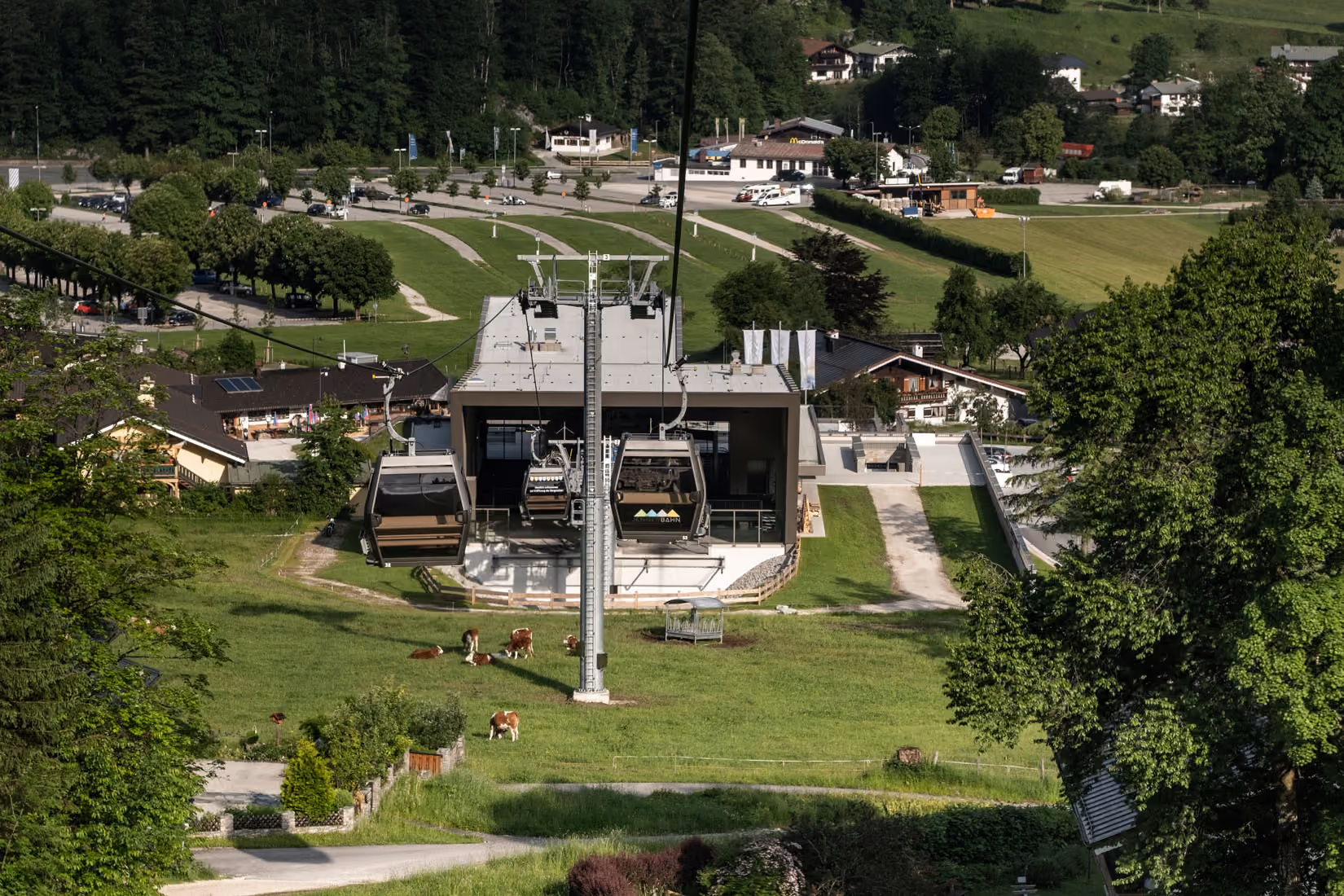 ennerbahn-Talstation mit Gondeln und grasenden Kühen im Sommer