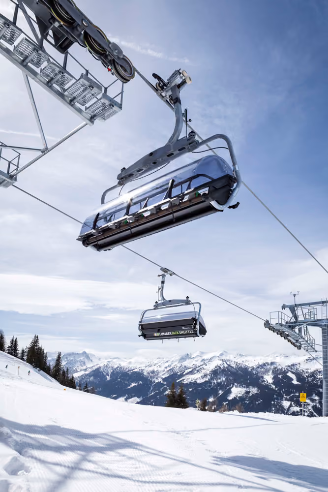 Zwei moderne Sessel mit Wetterschutzhaube der Lumberjack Shuttle Bahn schweben über verschneite Landschaft
