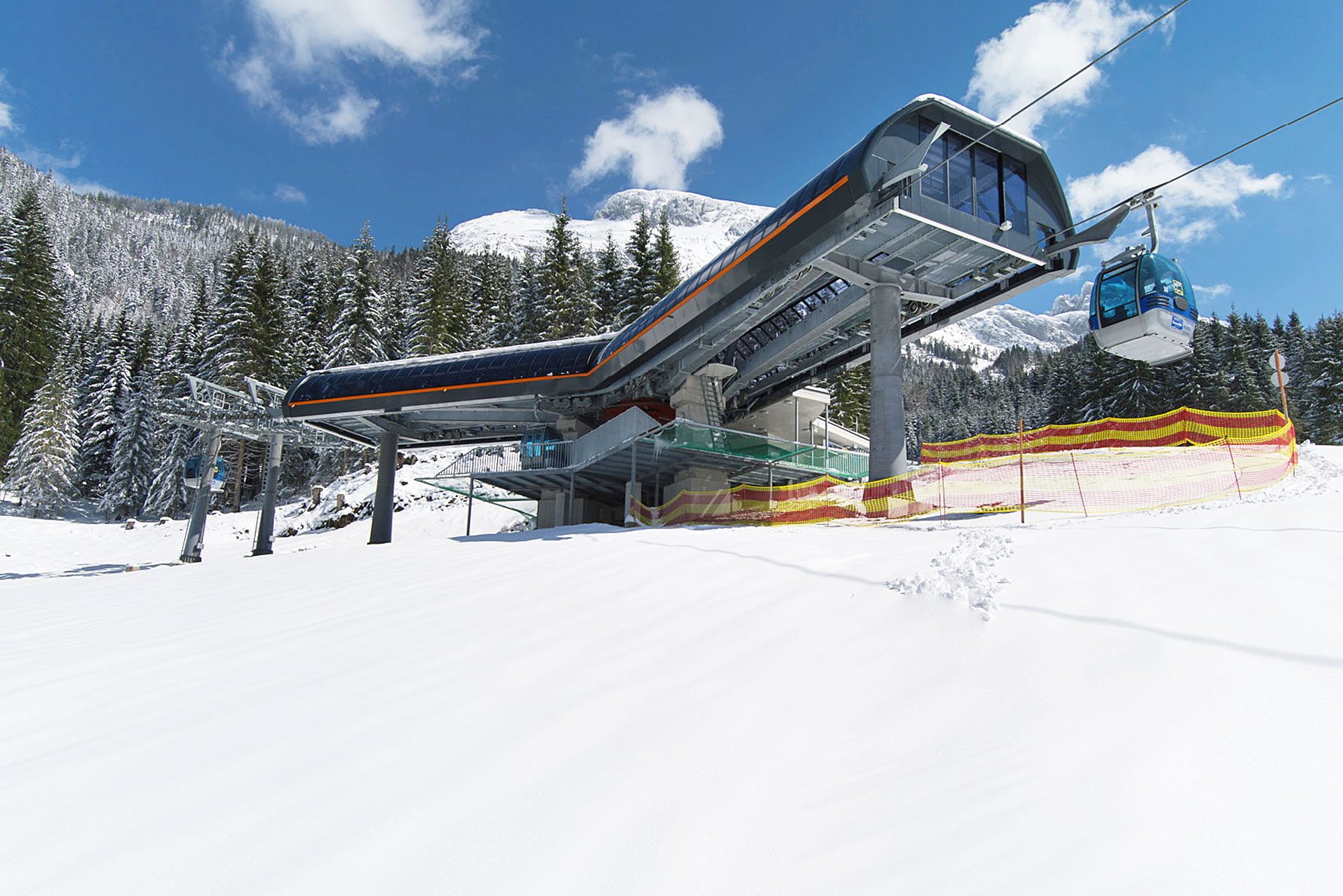 Moderne Talstation einer Kabinenbahn mit auffahrender Gondel im verschneiten Bergwald
