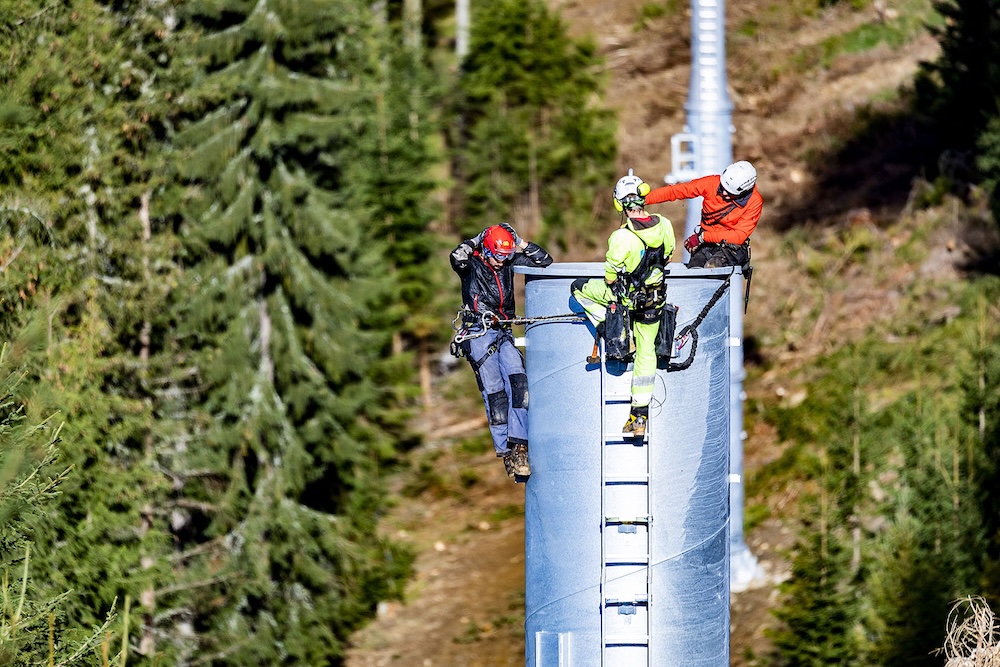 Drei Monteure sichern sich auf einer Seilbahnstütze im Wald