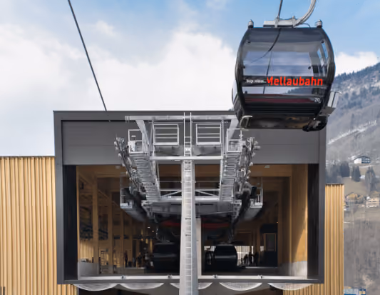Gondel der Mellaubahn fährt in moderne Talstation mit Holzfassade ein