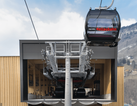 Gondel der Mellaubahn fährt in moderne Talstation mit Holzfassade ein