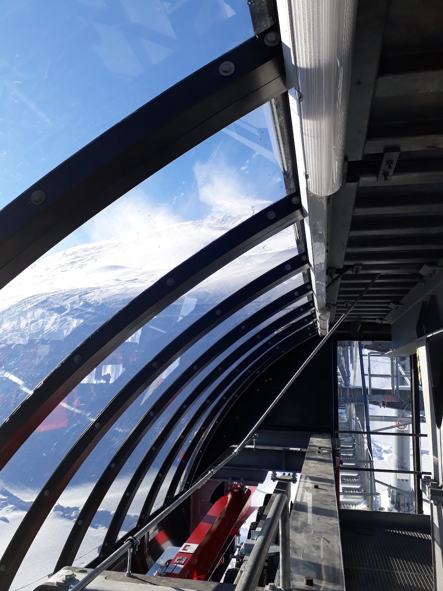 Transparente Dachkonstruktion einer Seilbahnstation mit Blick auf technische Komponenten und winterliche Landschaft