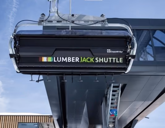 Frontansicht eines modernen 6er-Sessels mit Beschriftung „Lumberjack Shuttle“ an einer Bergstation von Doppelmayr
