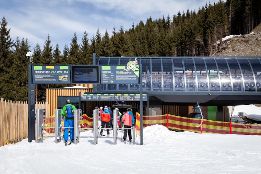 Einstiegsbereich der Lumberjack Shuttle Sesselbahn mit wartenden Wintersportler:innen vor moderner Talstation