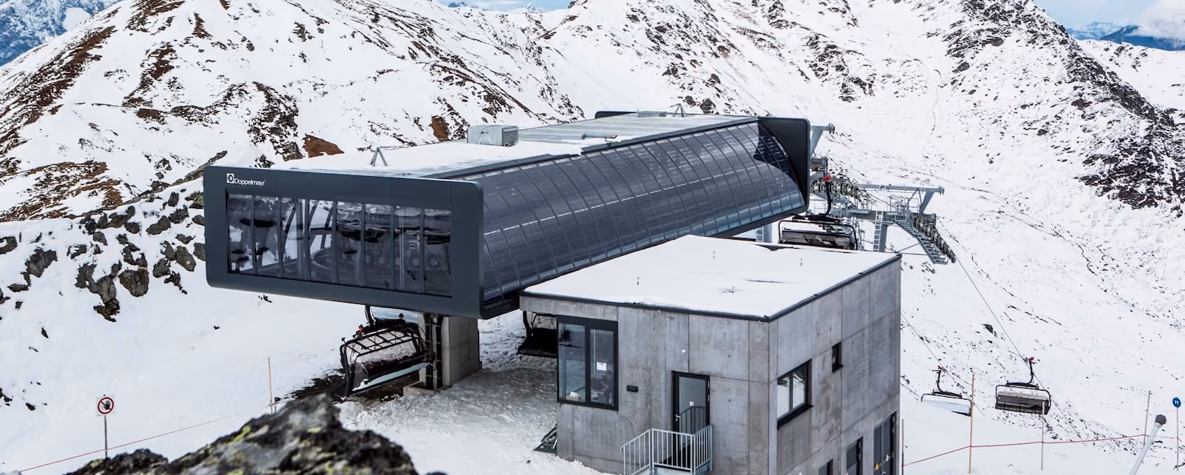 Moderne Bergstation mit gläserner Verkleidung und Betonbau von Doppelmayr inmitten verschneiter Hochgebirgslandschaft