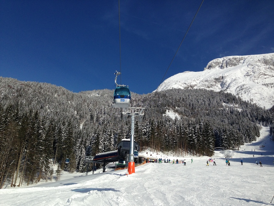 Auffahrende Gondel über der Talabfahrt mit Skifahrern und Bergkulisse