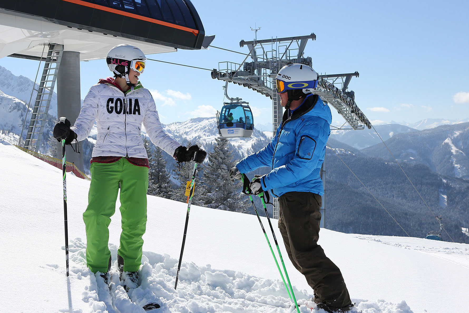 Zwei Skifahrer vor der Bergstation der Donnerkogelbahn mit Panoramablick