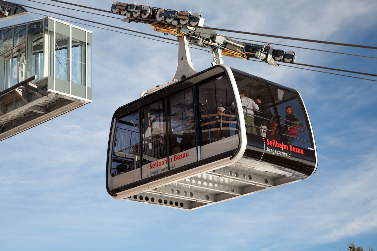 Kabine der Seilbahn Bezau mit Fahrgästen während der Fahrt vor blauem Himmel