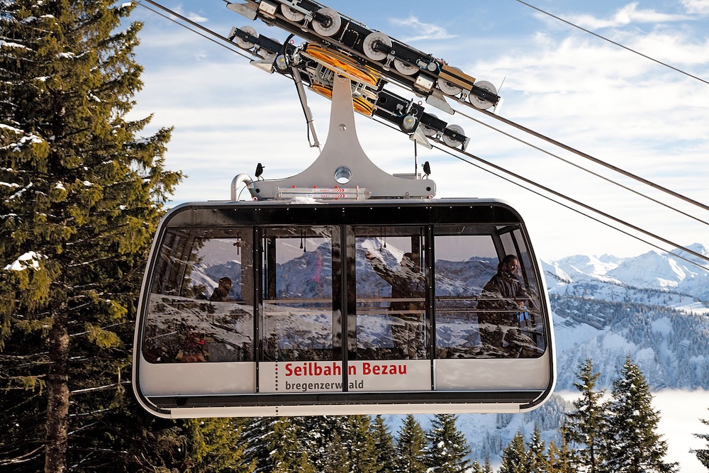 Gondel der Seilbahn Bezau schwebt durch verschneite Landschaft mit Bergen im Hintergrund