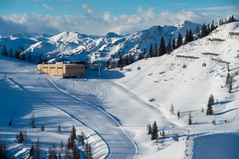 Moderne Bergstation im Skigebiet mit präparierter Piste und verschneiten Bergen im Hintergrund